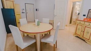 Un comedor con una mesa redonda, sillas blancas, un refrigerador y un mueble con diseño floral.