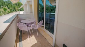 Un balcon avec une table ronde et quatre chaises, une fenêtre et une vue sur la verdure.