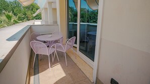 A balcony with a round table and four chairs, a window, and a view of greenery.