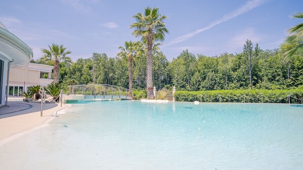 A swimming pool with a bridge, surrounded by palm trees and a forest.