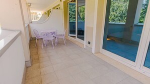 A balcony with a table and chairs, a sliding glass door, and a view of greenery.