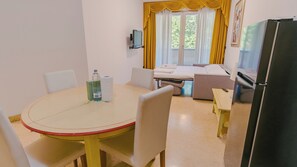 A hotel room with a dining table, chairs, a bed, a TV, and a refrigerator.
