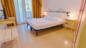 Quarto de hotel bem arrumado com cama, mesas de cabeceira, uma cadeira e escrivaninha.