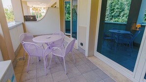 A patio with a round table and four chairs, a sliding glass door leading to an outdoor seating area, and a small window with a view of trees.