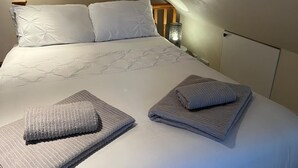 A neatly made bed with pillows and folded towels, a bedside lamp, and a wooden headboard. - Two Storey Annex (Cambridge)