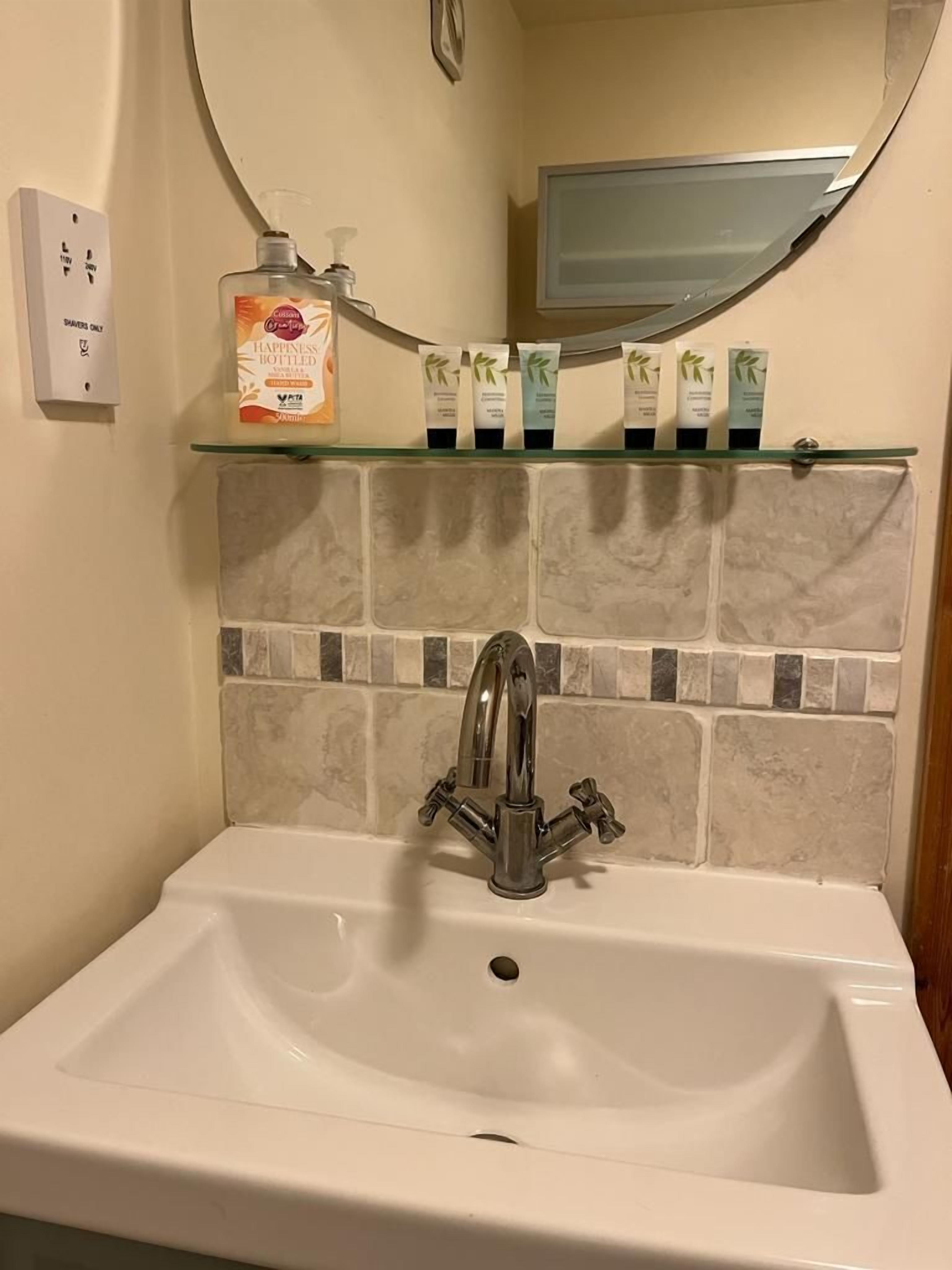 A bathroom with a white sink, a mirror above it, and a shelf with toiletries.
