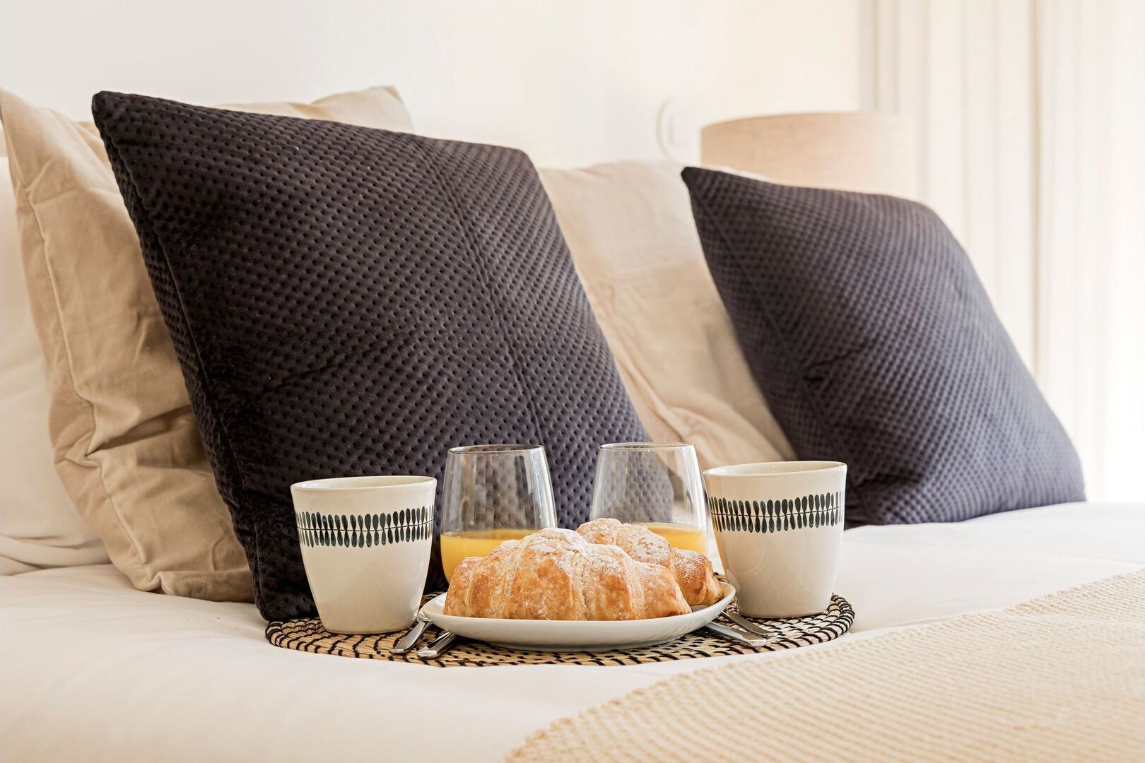 A bed with pillows, a plate of pastries, and two glasses of orange juice.
