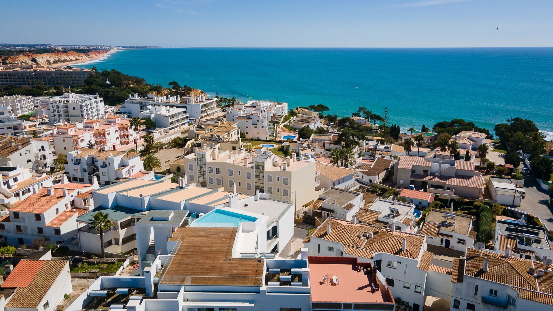 A coastal residential area with white buildings, a swimming pool, and a view of the sea.