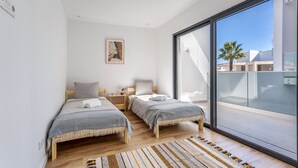 A modern bedroom with two single beds, a large sliding glass door to a balcony, and a patterned rug on the floor.