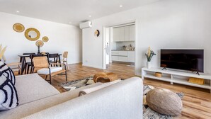 A modern living room with a sofa, dining area, kitchen, and TV.
