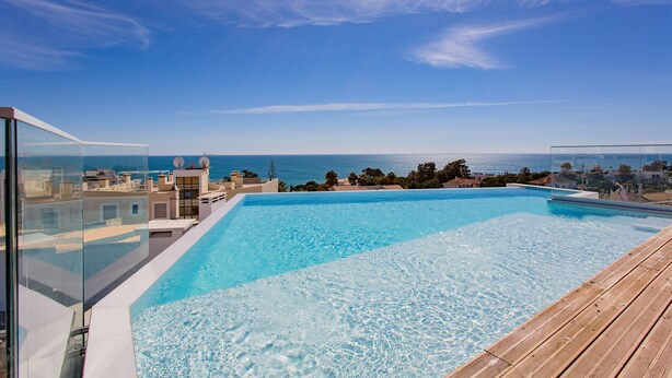 A rooftop infinity pool with a clear view of the ocean and distant buildings.