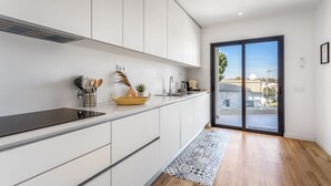 A modern kitchen with white cabinets, a black countertop, and a large sliding glass door leading to a balcony with a view of buildings.