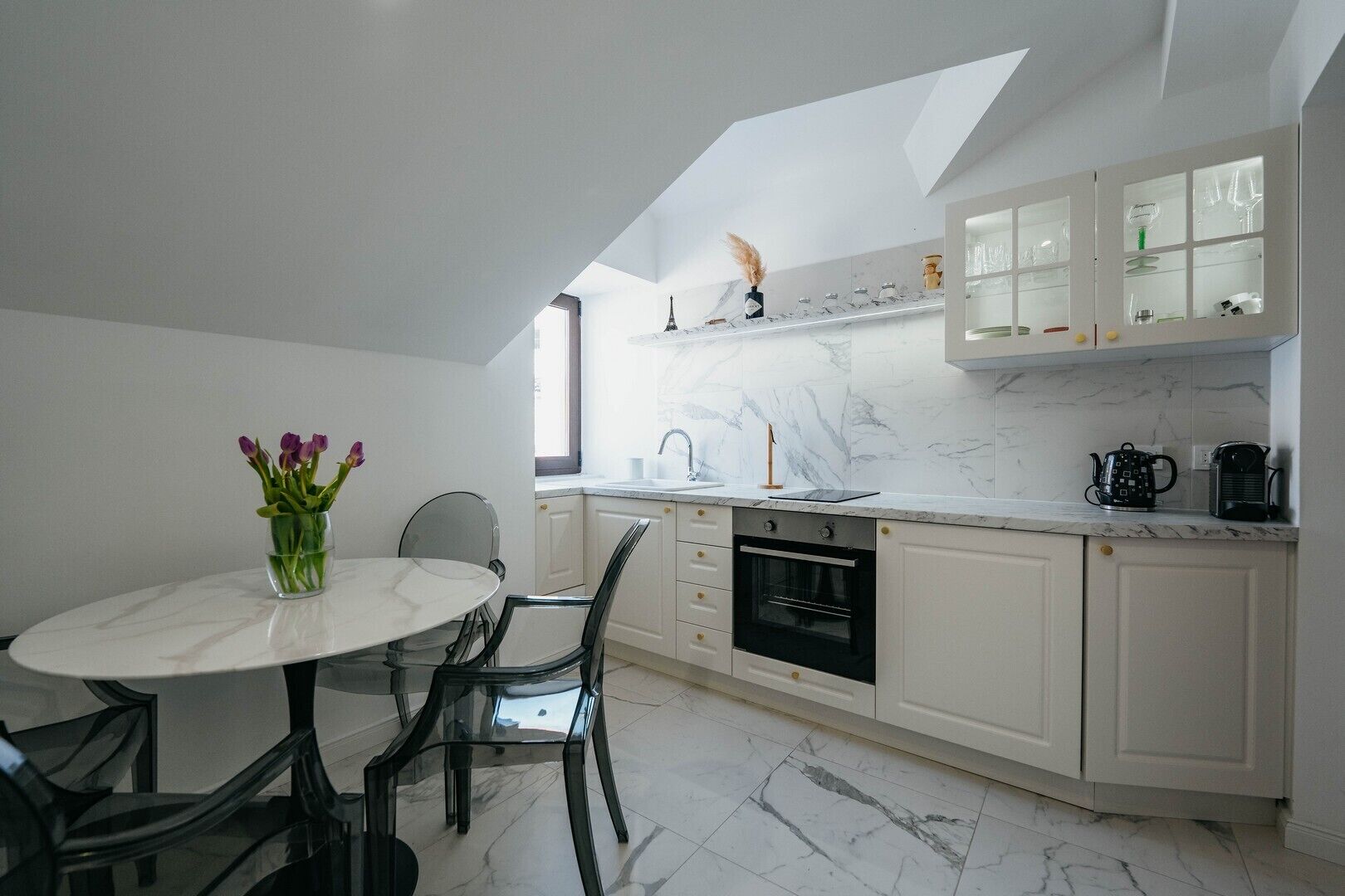 A modern kitchen with white cabinets, a marble countertop, and a built-in oven.