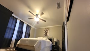 A bedroom with a bed, a nightstand, a lamp, a ceiling fan, and a window with curtains.