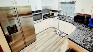 A modern kitchen with white cabinets, stainless steel appliances, a granite countertop, and a patterned rug.