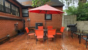 A patio with a brick floor, a red umbrella, and orange chairs.