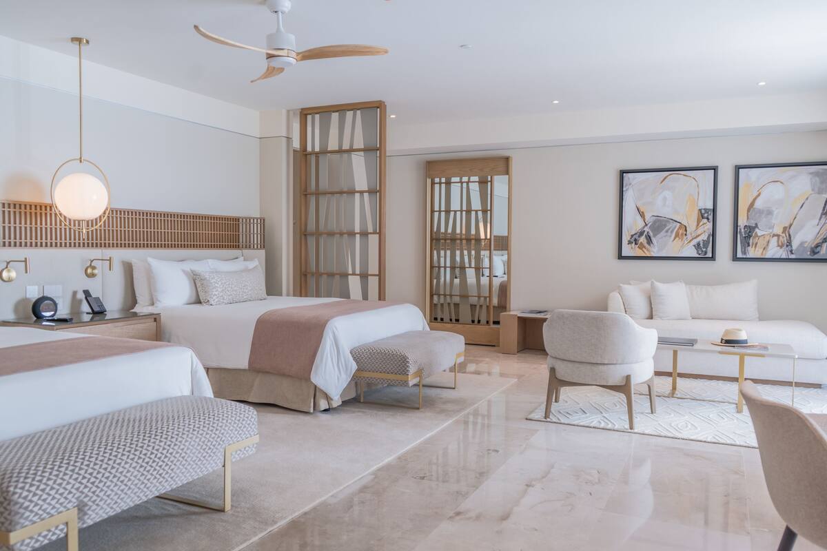 A modern hotel room with a large bed, a sofa, a desk, and a ceiling fan.