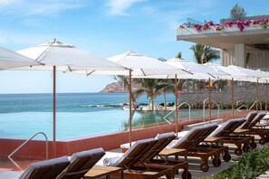 A poolside area with lounge chairs and umbrellas, overlooking a clear blue sea and a rocky coastline. - Grand Velas Boutique Hotel - Adults Only - All Inclusive (Cabo San Lucas)