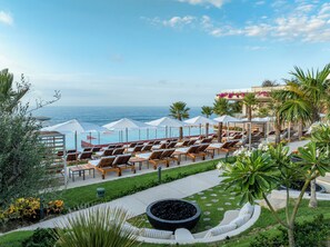 Un espace aménagé au bord de la piscine, avec des chaises longues et des parasols, offrant une vue sur l’océan.