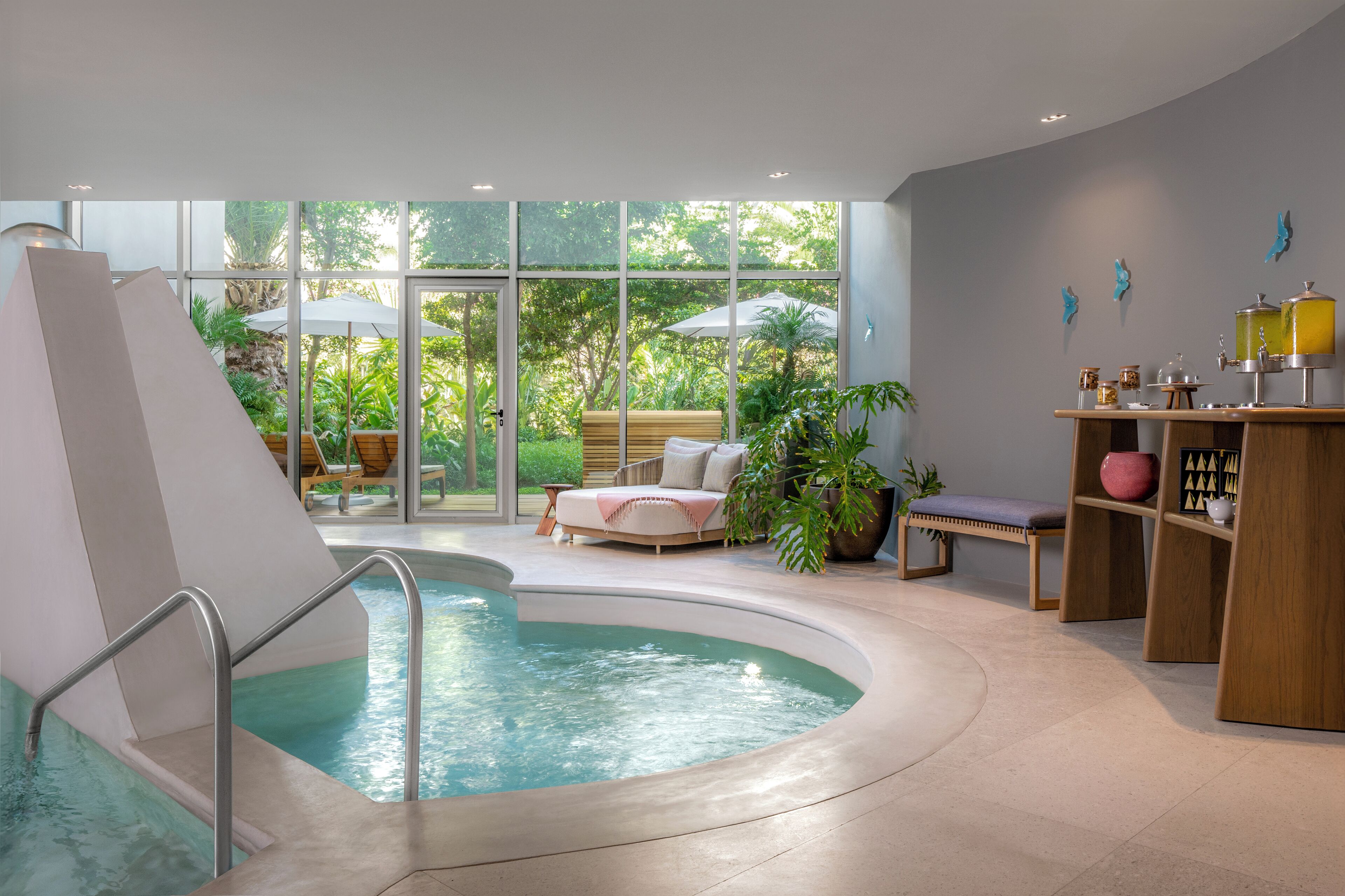A modern indoor pool area with a slide, seating, and a view of greenery outside.