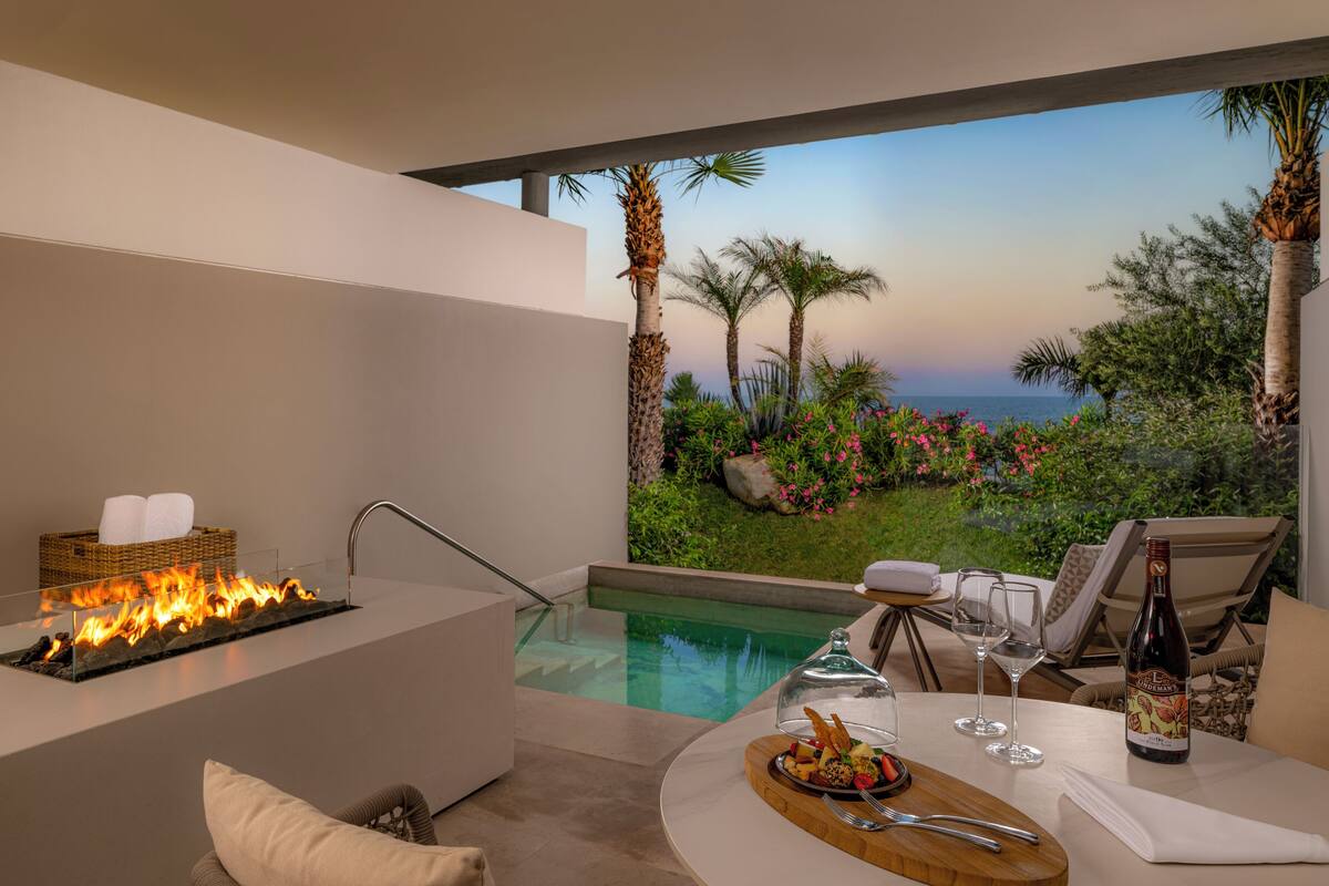A modern outdoor dining area with a pool, a fire feature, and a view of the ocean.