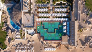 Vista aérea de un resort con una piscina grande, sombrillas de playa y una zona de playa.
