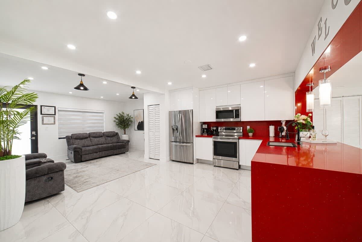Una cocina moderna con armarios blancos, electrodomésticos de acero inoxidable y encimera roja.