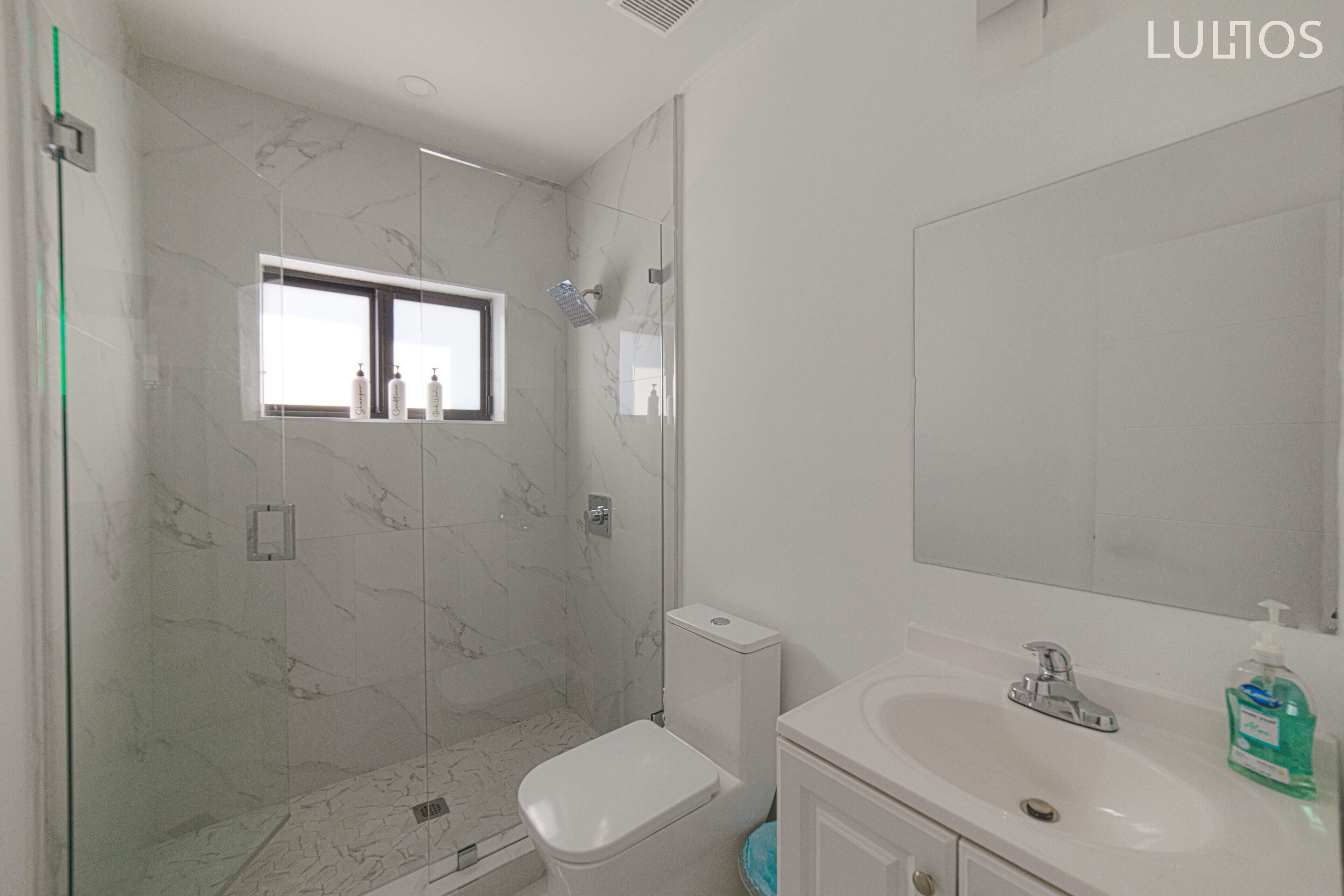 Une salle de bain moderne avec une douche à parois de verre, des toilettes, un lavabo avec un miroir et une fenêtre.