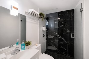 A modern bathroom with a glass-enclosed shower, a white sink with a mirror, and toiletries. - Modern Retreat • BBQ • Near South Beach & MIA (Miami)