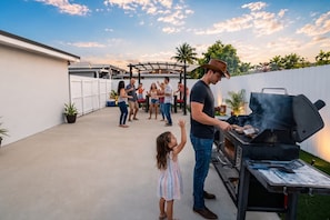 A patio area with a barbecue grill, potted plants, and a group of people gathered around. - Modern Retreat • BBQ • Near South Beach & MIA (Miami)