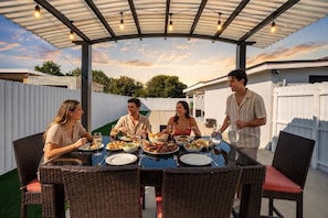 A covered outdoor dining area with wicker furniture and a table set for a meal. - Modern Retreat • BBQ • Near South Beach & MIA (Miami)