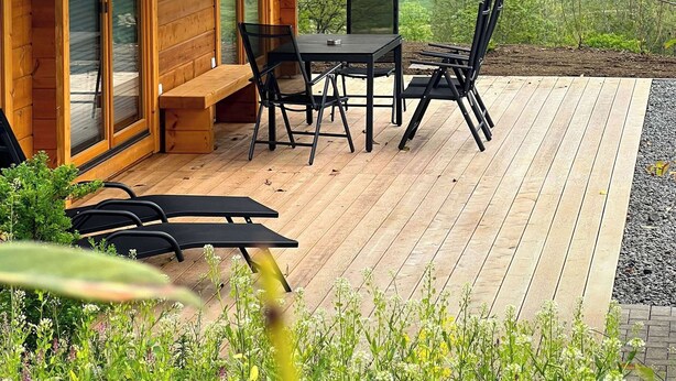 A wooden cabin with a deck, a table, and chairs.