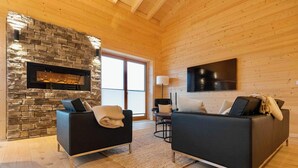 A modern living room with a stone fireplace, two black sofas, a coffee table, and a TV mounted on the wall.