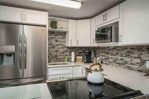 Kitchen features stainless steel appliances, white cabinetry, and a black stovetop.