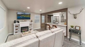 A modern living room with a fireplace, a sofa, a dining area, and a kitchen with a large mirror. - The Silver Elk House | Downtown Coeur d’Alene (Coeur d'Alene)