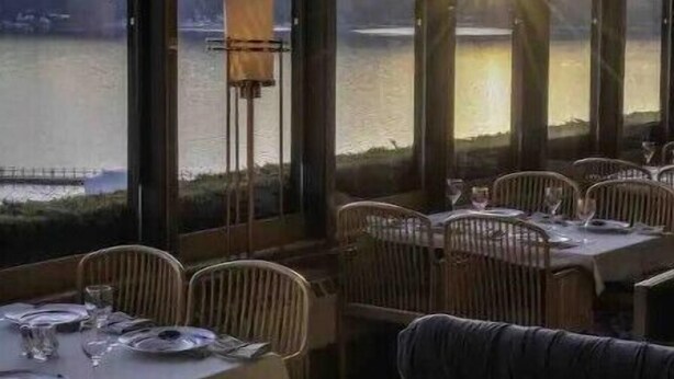 A restaurant with tables set for dining, large windows offering a view of a body of water and distant hills, and a cozy seating area with cushioned chairs. - The Silver Elk House | Downtown Coeur d’Alene (Coeur d'Alene)