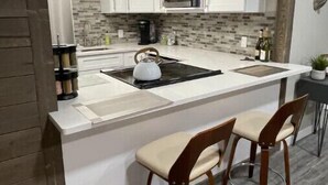 A modern kitchen with white cabinets, a black countertop, and two wooden bar stools. - The Silver Elk House | Downtown Coeur d’Alene (Coeur d'Alene)