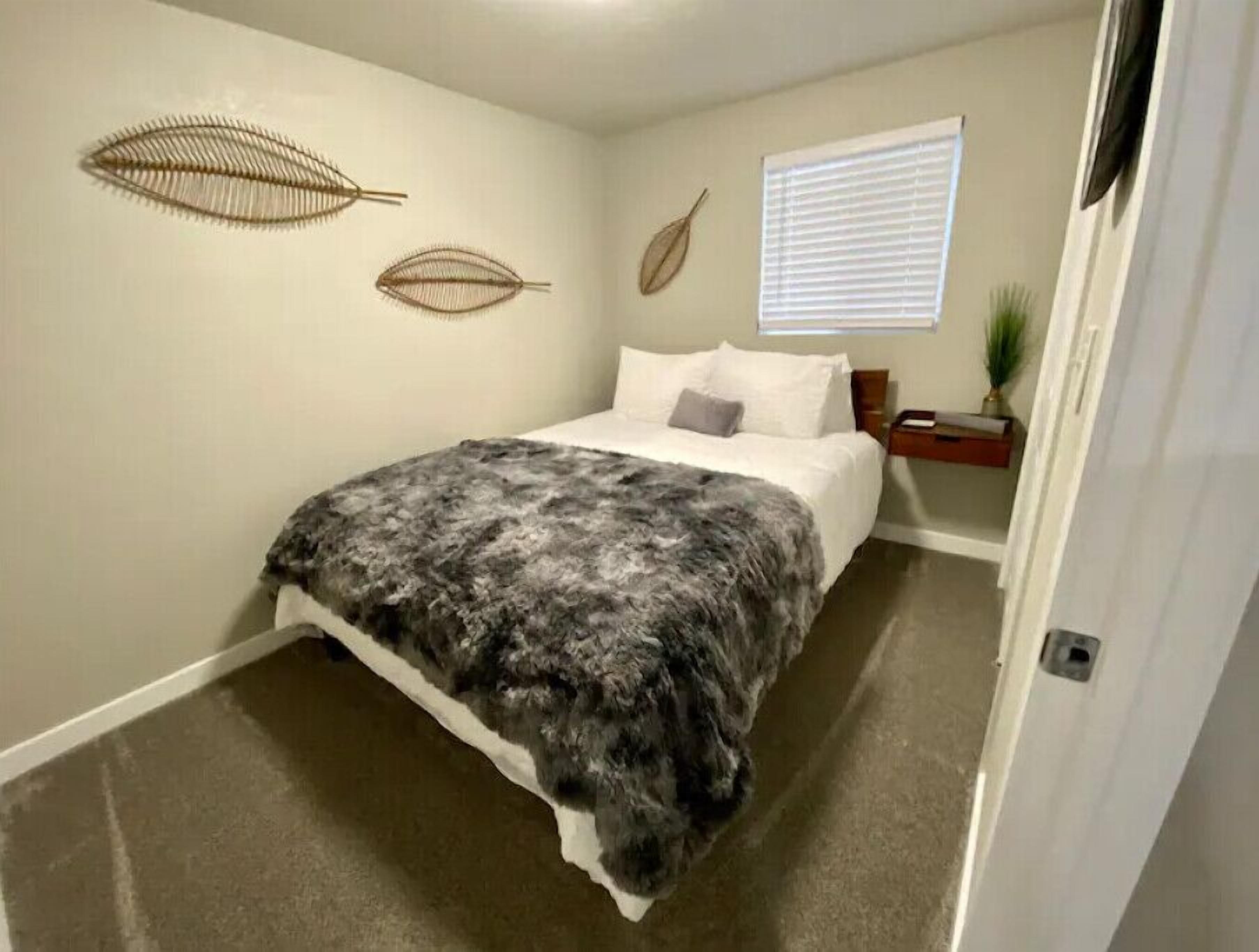 A bedroom with a bed, a nightstand, a window with blinds, and wall art.
