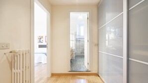 A hallway with a radiator, a door leading to a bathroom, and a view into a bedroom.