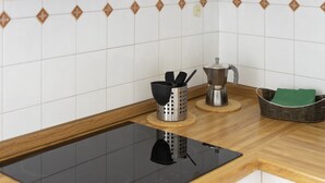 A kitchen with a black induction cooktop, a stainless steel coffee maker, a metal strainer, and a wicker basket with a green cloth.