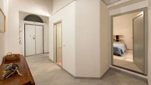 A hallway with a wooden bench, a basket, and a door leading to a bedroom with a bed and a nightstand. - San Zanobi 33 - One Bedroom Apartment, Sleeps 2 (Firenze)