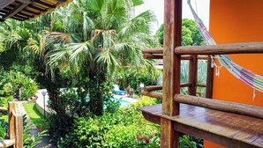 Terraza de madera con hamaca, rodeada de exuberante vegetación tropical y una zona de piscina.