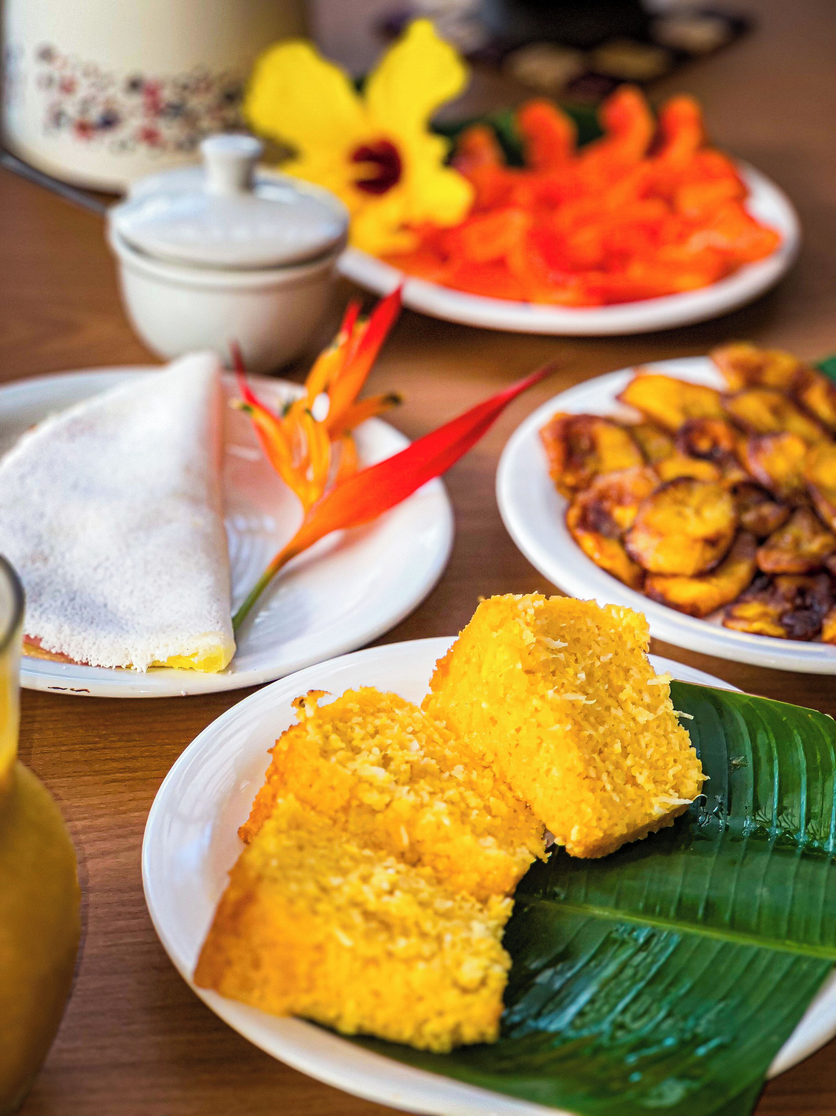 A table with various dishes, including a banana leaf dish, a plate with fried items, and a bowl with a yellow condiment.
