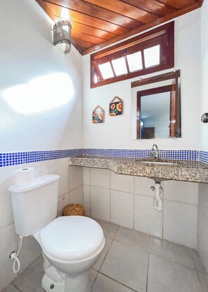 Un baño con inodoro, lavamanos y ventana sobre el espejo.