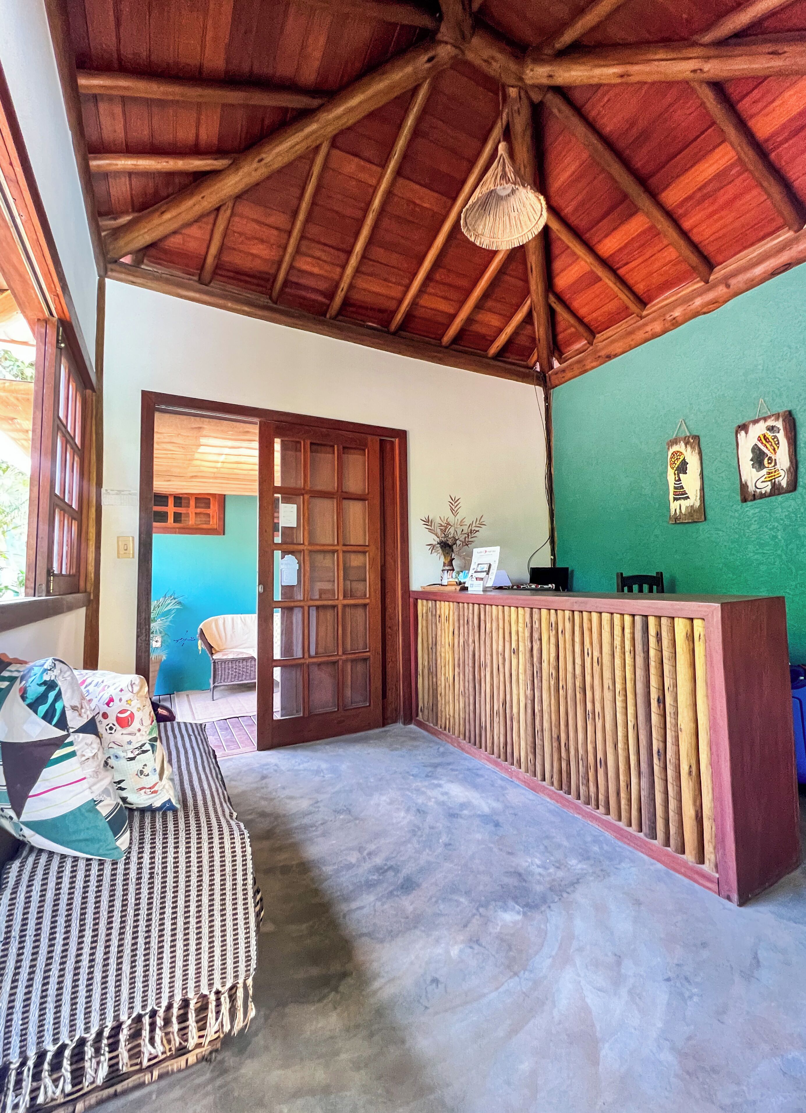 Uma área de recepção com balcão de madeira, um banco de fibra natural e uma parede verde.