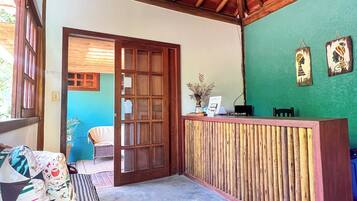 Uma área de recepção com balcão de madeira, um banco de fibra natural e uma parede verde.