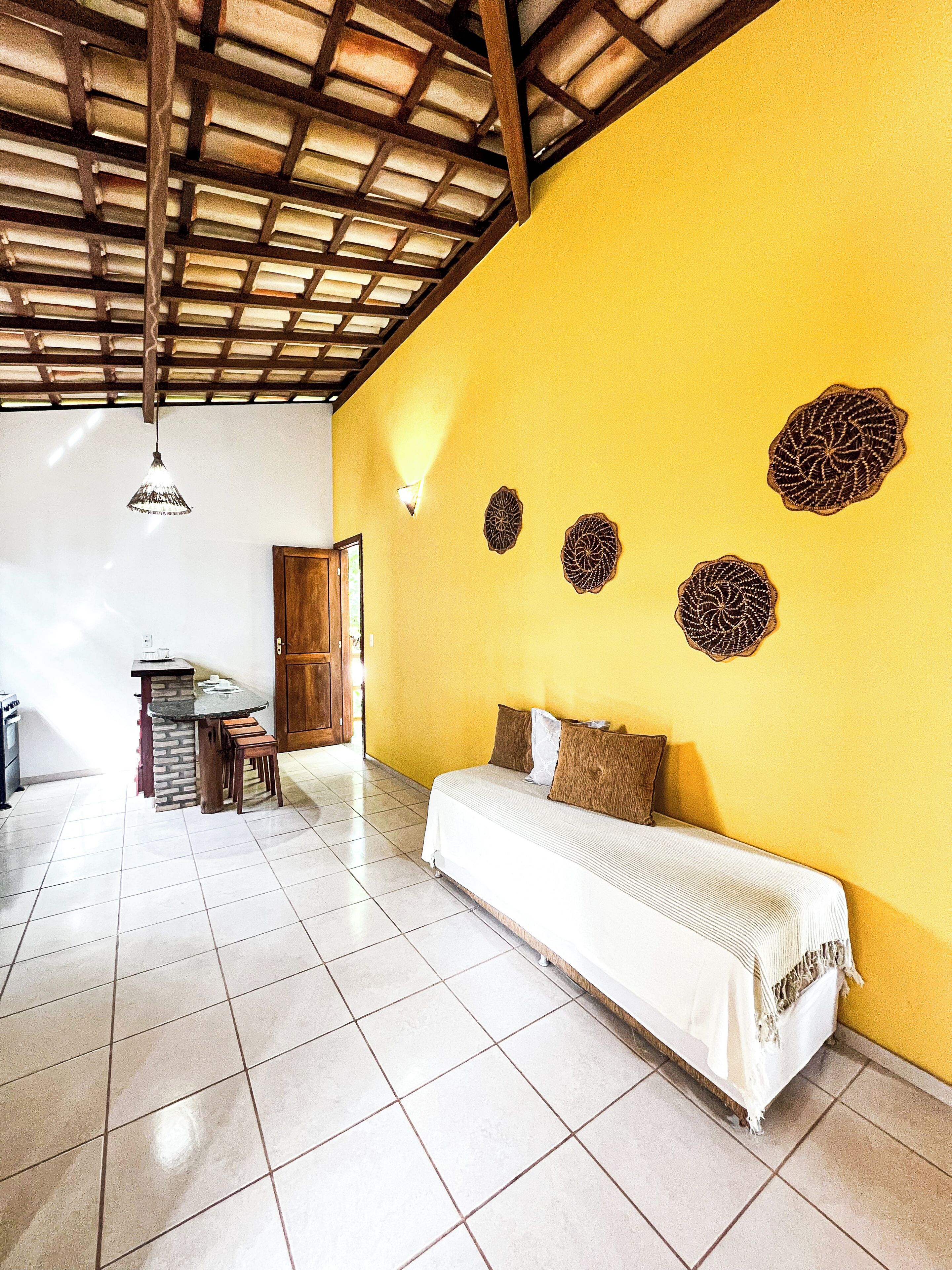 Een kamer met een gele wand, een houten plafond, een bed, een tafel met stoelen en decoratieve wandkunst.