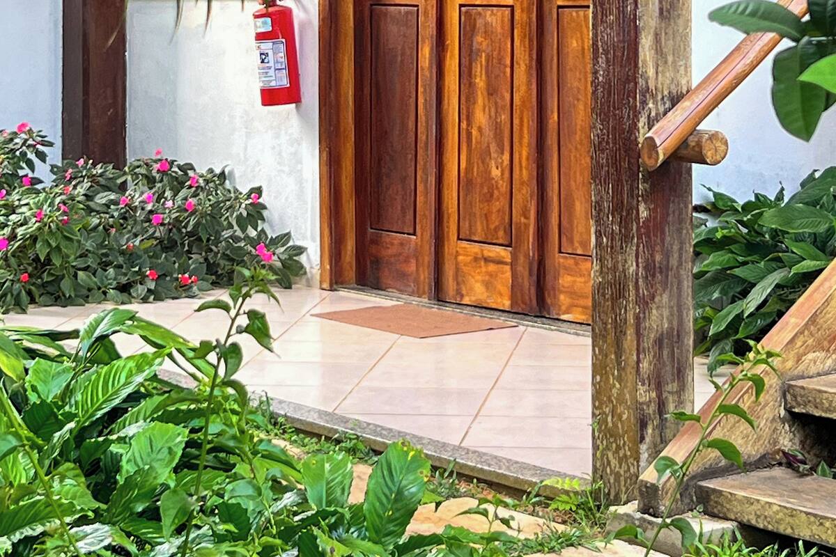 A wooden door with glass panels, a fire extinguisher, and a small garden with pink flowers.