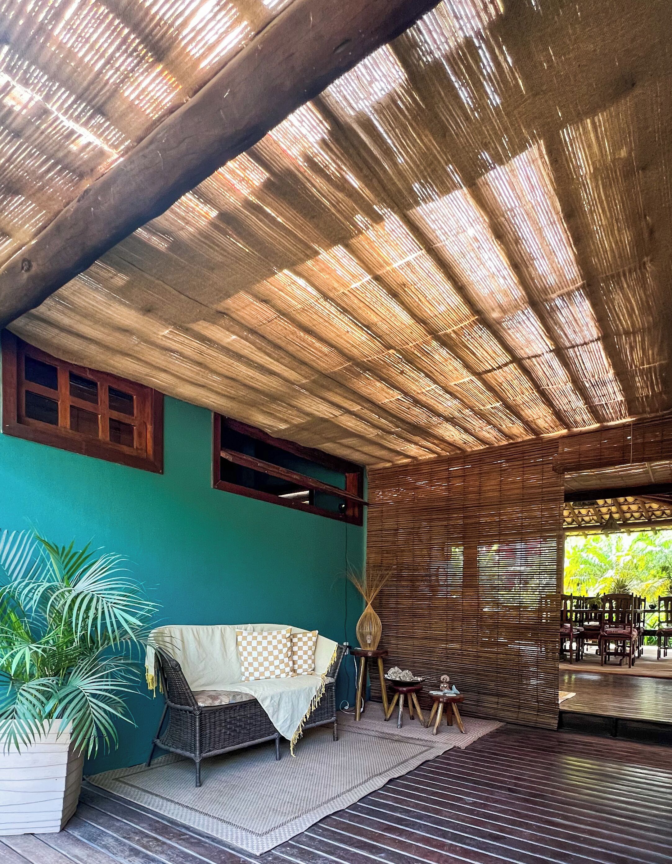 A covered outdoor seating area with a woven ceiling, a sofa, and a dining table.