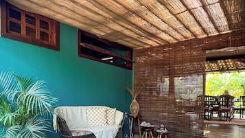 A covered outdoor seating area with a woven ceiling, a sofa, and a dining table.